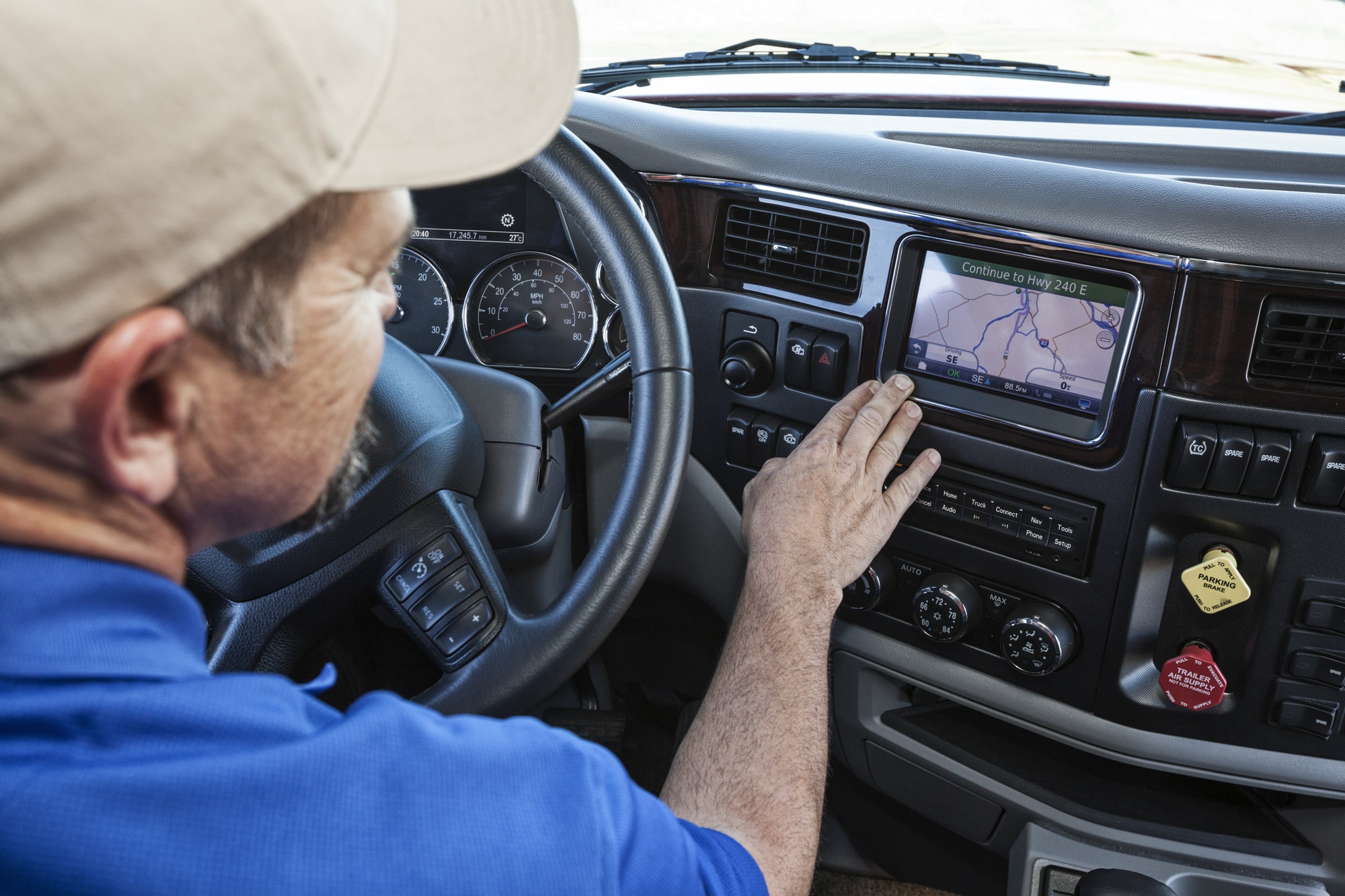 Driver parked by the side of the road using a GPS mapping device in the cab of a commercial truck.